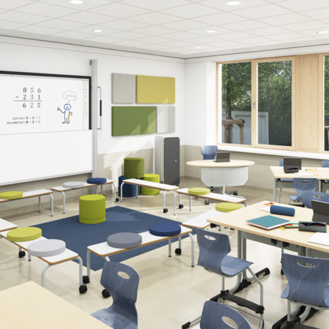 Klassenraum einer Grundschule mit gruppierten Schülertischen, Akustikelementen an den Wänden und einem Sitzkreis aus Bänken