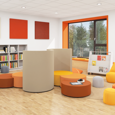 Schulbibliothek mit Bücherregalen an den Wänden und einer Gruppe aus Polsterelementen in der Mitte
