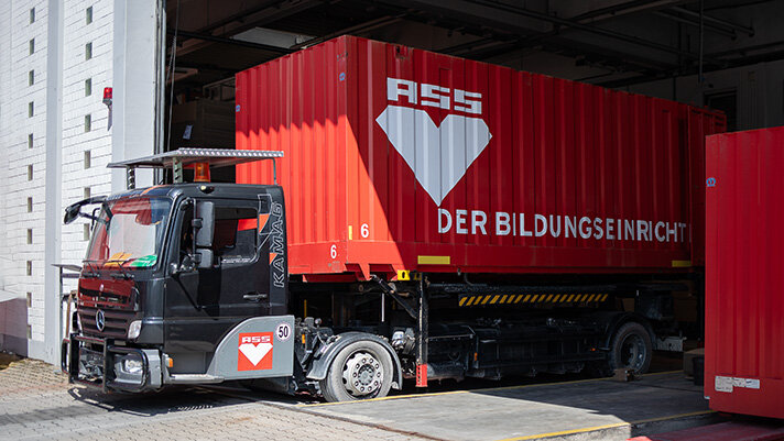 service-lieferung-montage Anfahrender LKW mit rotem Container und ASS-Einrichtungssysteme GmbH-Logo
